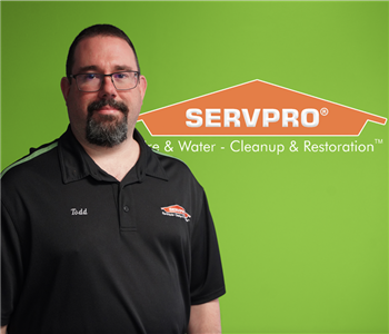 A man in a SERVPRO shirt smiling at the camera with a green backdrop and a SERVPRO logo